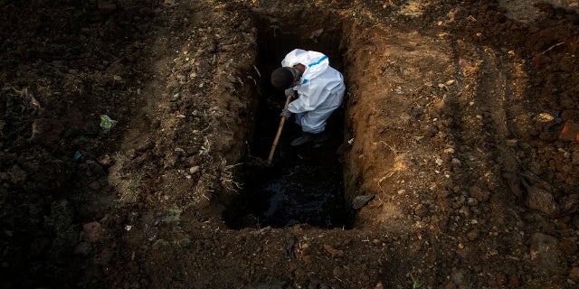 A man in protective gear digs the earth to bury the body of a person who died of COVID-19 in Gauhati, India on April 25. (AP)