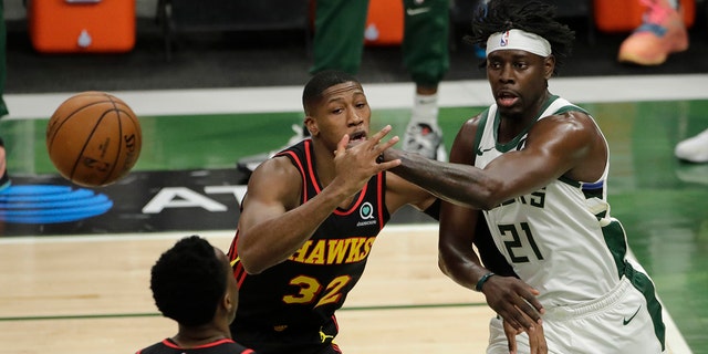 Milwaukee Bucks' Jrue Holiday, right, passes the ball past Atlanta Hawks' Kris Dunn, left, during the first half of Game 5 of the NBA Eastern Conference Finals Thursday, July 1, 2021, in Milwaukee. (AP Photo/Aaron Gash)