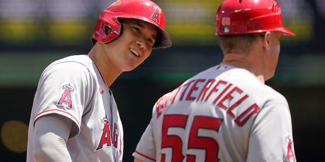 Los Angeles Angels' Shohei Ohtani, left, talks with third base coach Brian Butterfield while on base during the first inning of a baseball game against the Seattle Mariners, Sunday, July 11, 2021, in Seattle. (AP Photo/Ted S. Warren)