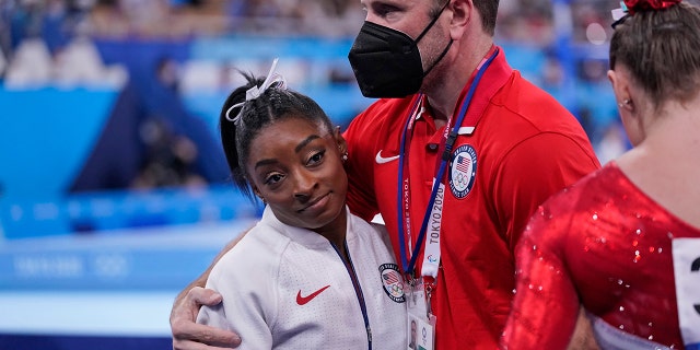 Coach Laurent Landi embraces Simone Biles after she exited the team final with apparent injury at the 2020 Summer Olympics, Tuesday, July 27, 2021, in Tokyo. The 24-year-old reigning Olympic gymnastics champion Biles huddled with a trainer after landing her vault. She then exited the competition floor with the team doctor. (AP Photo/Gregory Bull)