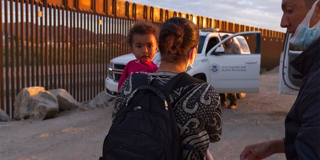 In this June 10, 2021, file photo, a migrant family from Brazil waits to be processed by U.S. Border Patrol agents after passing through a gap in the border wall from Mexico in Yuma, Arizona. 