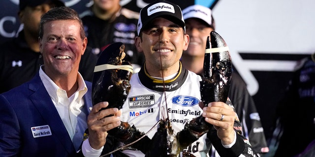 Aric Almirola smiles as he wields a giant lobster after winning the NASCAR Cup Series car race on Sunday July 18, 2021 in Loudon, NH.  At left is Dave McGrath, General Manager of New Hampshire Motor Speedway.  (AP Photo / Charles Krupa)
