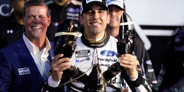 Aric Almirola smiles as he holds up a giant lobster after winning the NASCAR Cup Series auto race Sunday, July 18, 2021, in Loudon, N.H. At left is Dave McGrath, general manager of New Hampshire Motor Speedway. (AP Photo/Charles Krupa)