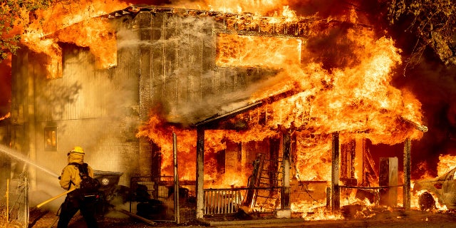 A firefighter sprays water while trying to stop the Sugar Fire, part of the Beckwourth Complex Fire, from spreading to neighboring homes in Doyle, Calif., Saturday, July 10, 2021. Pushed by heavy winds amid a heat wave, the fire came out of the hills and destroyed multiple residences in central Doyle. (AP Photo/Noah Berger)