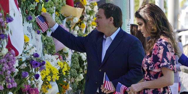 Florida Gov. Ron DeSantis, left, and his wife Casey leave flags at a makeshift memorial near the Champlain Towers South condo building, where scores of victims remain missing more than a week after it partially collapsed, Saturday, July 3, 2021, in Surfside, Fla. 