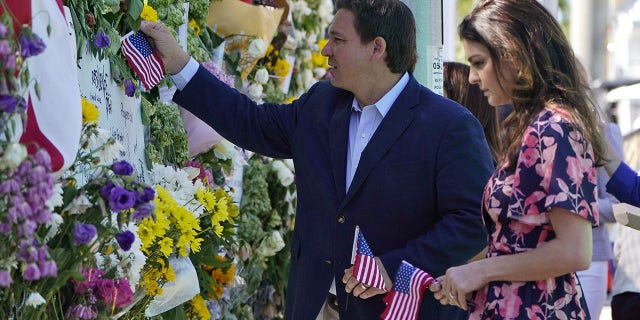 Florida Gov. Ron DeSantis, left, and his wife Casey leave flags at a makeshift memorial near the Champlain Towers South condo building, where scores of victims remain missing more than a week after it partially collapsed, Saturday, July 3, 2021, in Surfside, Fla.