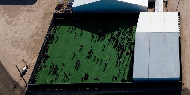 Migrants in a green area outside of a soft-sided detention center after they were taken into custody while trying to sneak into the U.S., in Donna, Texas, in March. (Associated Press)