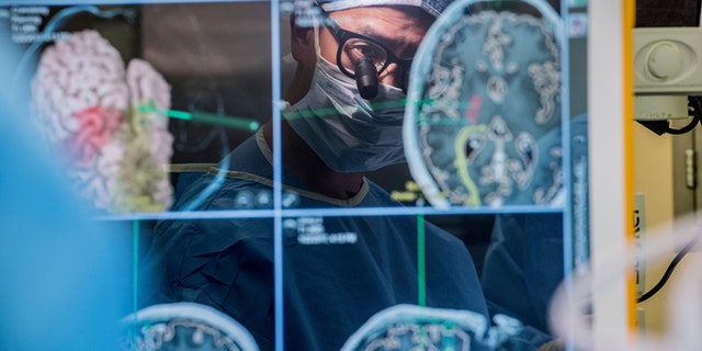 In this 2017 photo provided by the University of California, San Francisco, neurosurgeon Dr. Edward Chang is reflected in a computer screen displaying scans of the brain as he performs surgery at UCSF. 
