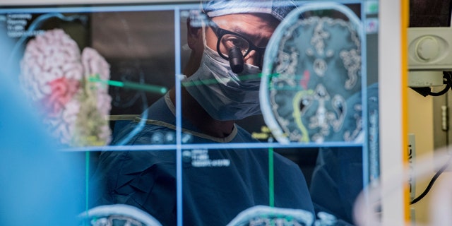 In this 2017 photo provided by the University of California, San Francisco, neurosurgeon Dr. Edward Chang is reflected in a computer monitor displaying brain scans as he performs surgery at UCSF. 