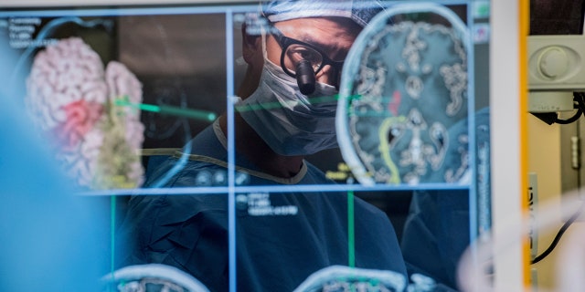 In this 2017 photo provided by the University of California, San Francisco, neurosurgeon Dr. Edward Chang is reflected in a computer screen displaying scans of the brain as he performs surgery at UCSF. 