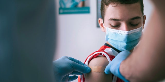 Doctor putting adhesive bandage to a teenage boy after Covid-19 vaccine injection.