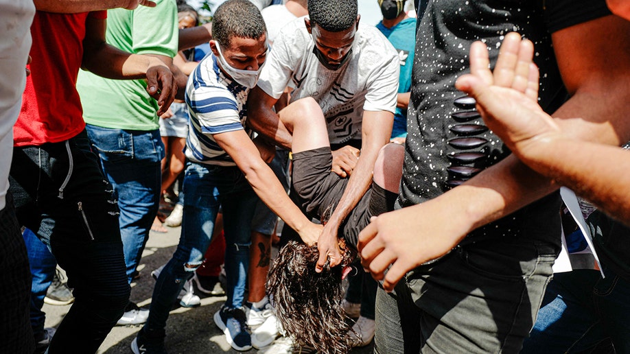 A man is seized by his neck during a demonstration against the government of Cuban President Miguel Diaz-Canel in Havana, on July 11, 2021. - Thousands of Cubans took part in rare protests Sunday against the communist government, marching through a town chanting "Down with the dictatorship" and "We want liberty." (Photo by ADALBERTO ROQUE / AFP) (Photo by ADALBERTO ROQUE/AFP via Getty Images)