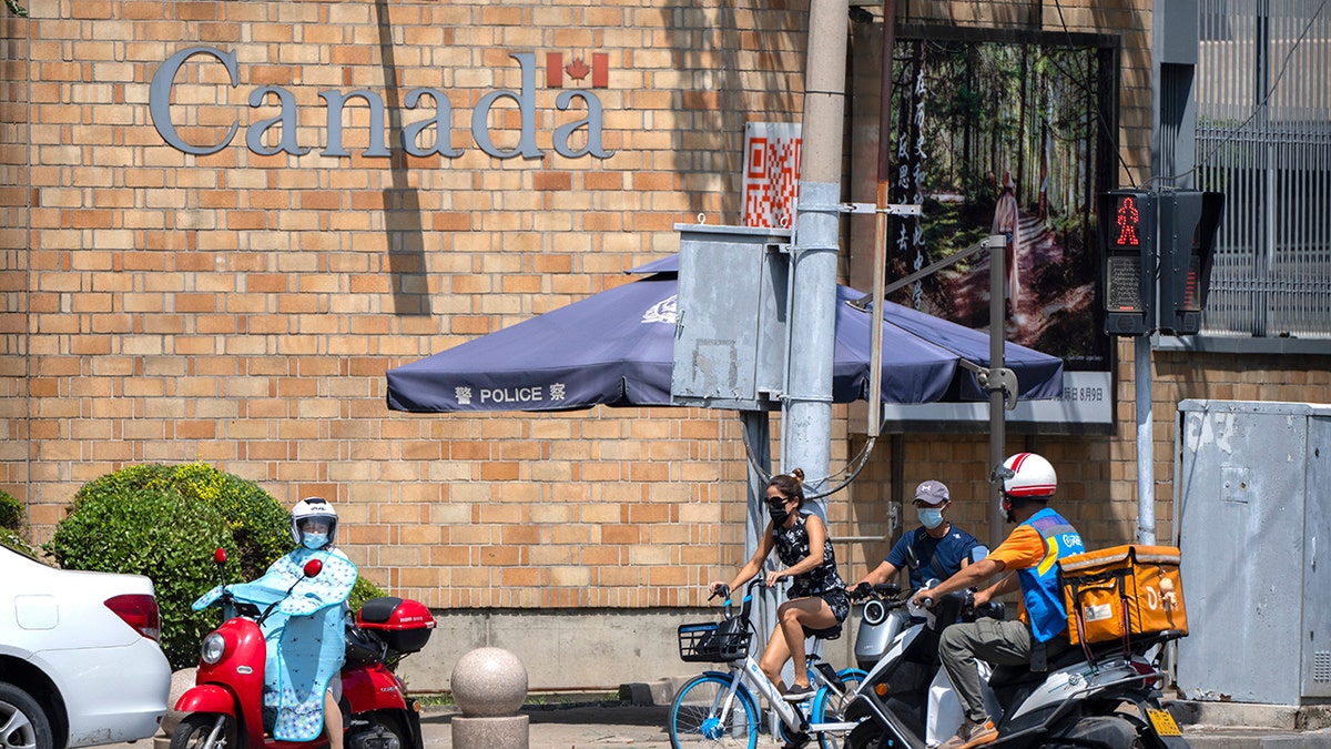 People wait to cross an intersection near of the Canadian Embassy in Beijing, Tuesday, Aug. 10, 2021. (AP Photo/Mark Schiefelbein)