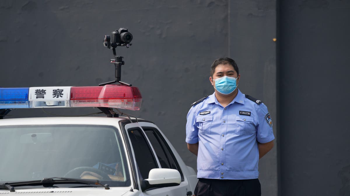 A policeman wearing a face mask stands guard next to a police vehicle with a camera outside a detention center where Dominic Barton, ambassador of Canada to China will meet Canadian Michael Spavor, in Dandong, China, Wednesday, Aug. 11, 2021. A Chinese court has sentenced Michael Spavor to 11 years on spying charges in case linked to Huawei. (AP Photo/Ng Han Guan)