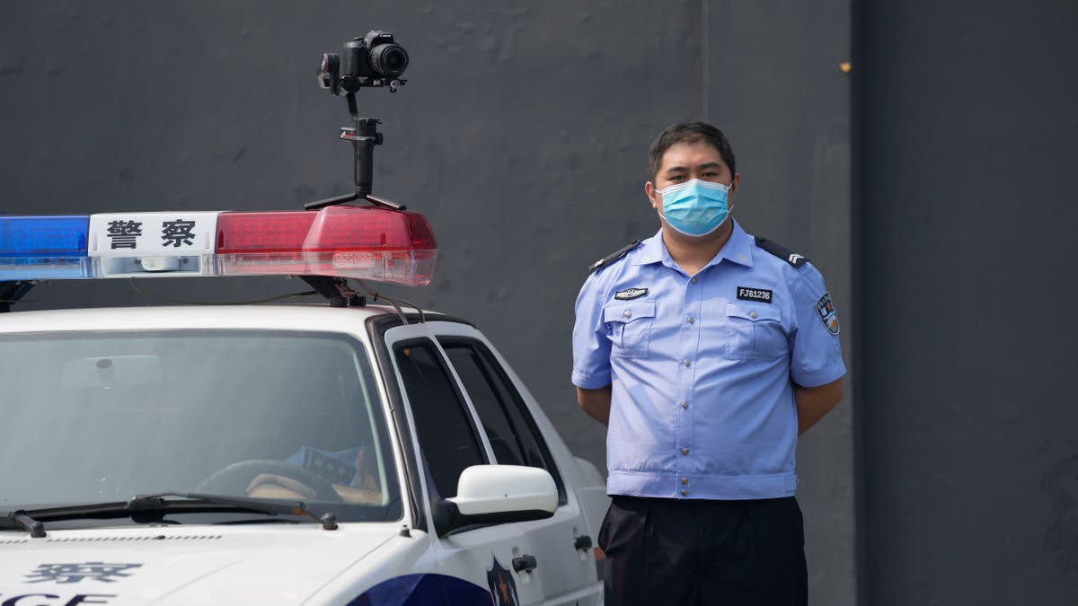 A policeman wearing a face mask stands guard next to a police vehicle with a camera outside a detention center where Dominic Barton, ambassador of Canada to China will meet Canadian Michael Spavor, in Dandong, China, Wednesday, Aug. 11, 2021. A Chinese court has sentenced Michael Spavor to 11 years on spying charges in case linked to Huawei. (AP Photo/Ng Han Guan)