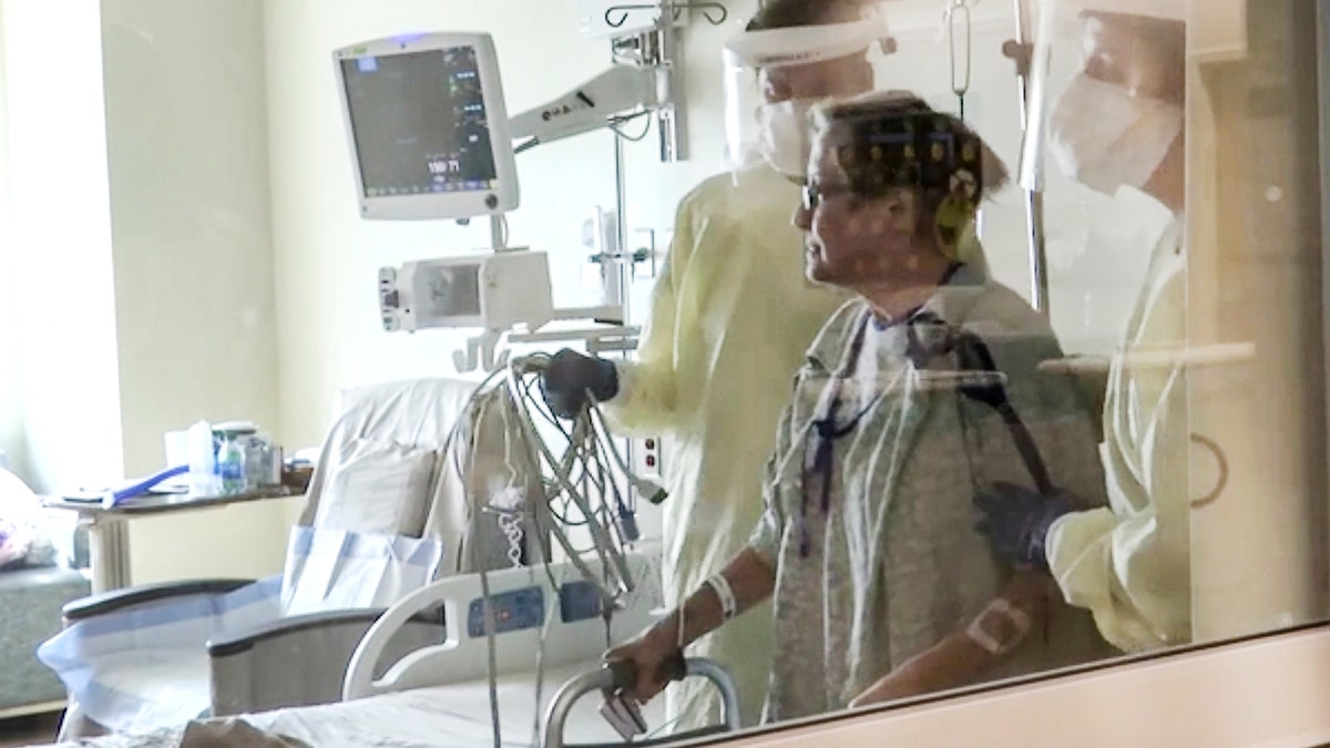 Coronavirus patient Joan Bronson walks across her hospital room with the help of a physical therapist at Ochsner Medical Center in the New Orleans suburb of Jefferson, La., on Tuesday, Aug.11, 2021. (AP Photo/Stacey Plaisance)