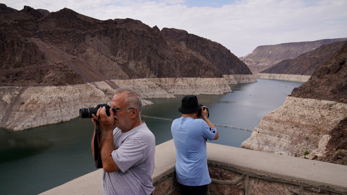People take pictures of Lake Mead near Hoover Dam at the Lake Mead National Recreation Area, Friday, Aug. 13, 2021, in Arizona. The bathtub ring of light minerals shows the high water mark of the reservoir which has fallen to record lows. (AP Photo/John Locher)