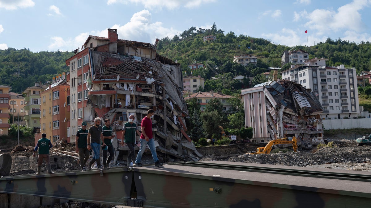 People walk on a temporary bridge set up by military in Bozkurt town of Kastamonu province, Turkey, Sunday, Aug. 15, 2021, after flooding. Turkey sent ships to help evacuate people and vehicles from a northern town on the Black Sea that was hard hit by flooding, as the death toll in the disaster rose Sunday to at least 62 and more people than that remained missing. (AP Photo)