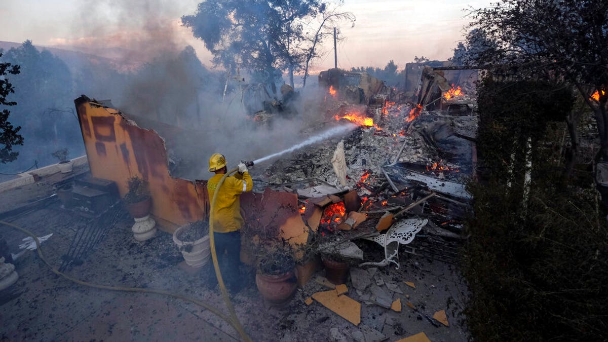 A firefighter tries to extinguish the flames at a burning house as the South Fire burns in Lytle Creek, San Bernardino County, north of Rialto, Calif., Wednesday, Aug. 25, 2021. 