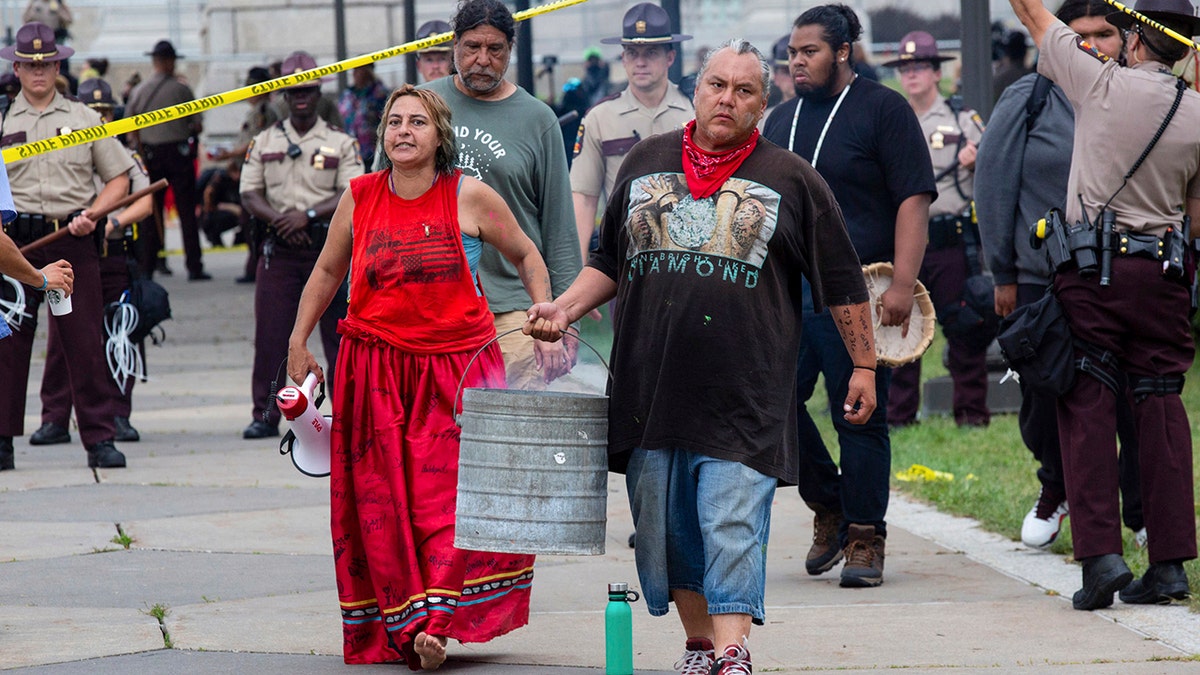 Two activists, who identify as water protectors, carry away the coals of a ceremonial fire after being removed from the site of a protest opposing the Enbridge Line 3 oil pipeline at the Minnesota Statehouse in St. Paul, Minn., Friday, Aug. 27, 2021. (Associated Press)