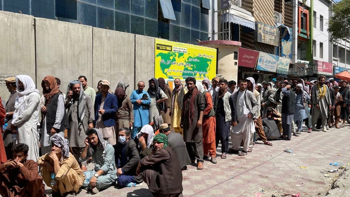 Afghans line up outside a bank to take out cash as people keep waiting at Hamid Karzai International Airport to leave the country after Taliban's takeover in Kabul, Afghanistan, on August 25, 2021.