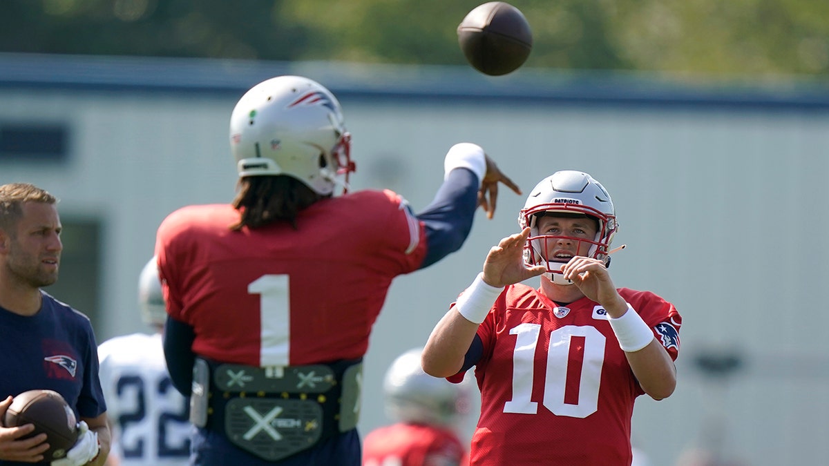 New England Patriots quarterback Cam Newton (1) passes the ball to Patriots quarterback Mac Jones (10) during a joint NFL football practice with the New York Giants, Thursday, Aug. 26, 2021, in Foxborough, Massachusetts.