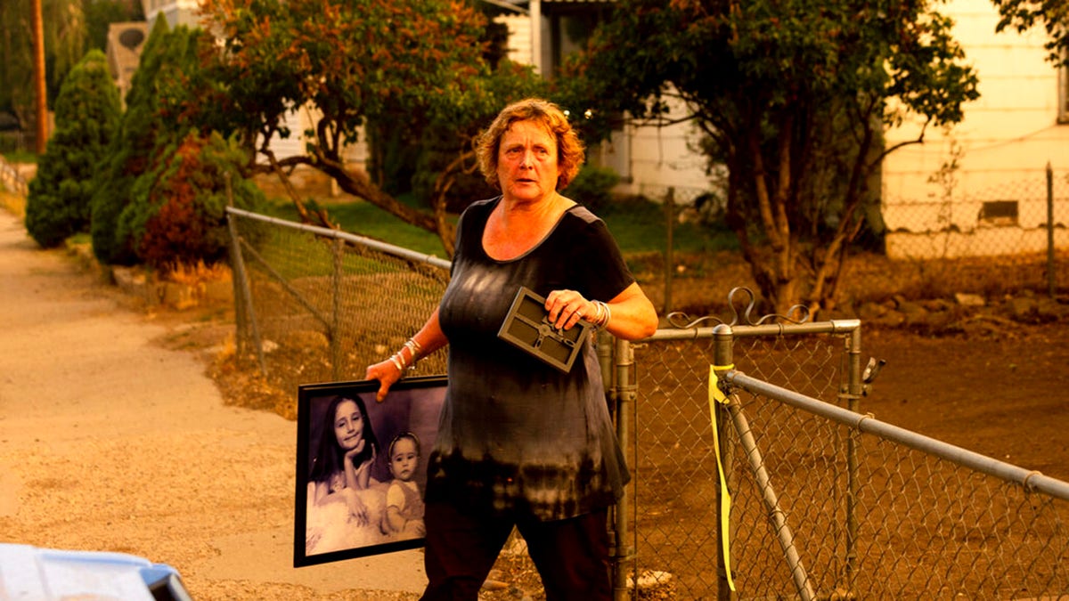 Rose Mooney carries photos from her home, which is under an evacuation warning, as the Dixie Fire burns towards Susanville, Calif., on Monday, Aug. 16, 2021.