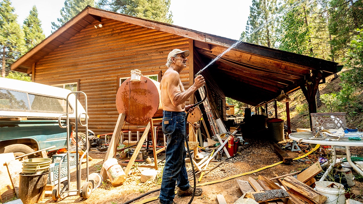 Dan Santos sprays water while defending his girlfriend's Greenville home as the Dixie Fire burns nearby in Plumas County, Calif., on Tuesday, Aug. 3, 2021. Dry and windy conditions have led to increased fire activity as firefighters battle the blaze which ignited July 14.?