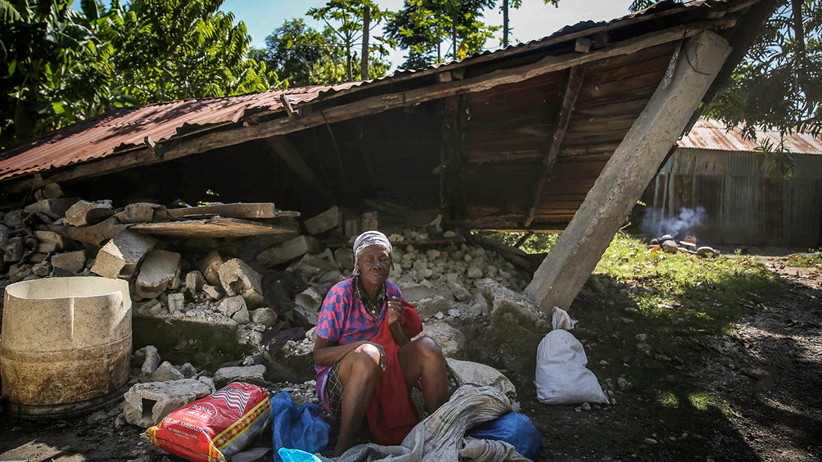 A woman sits in front of a destroyed house after the earthquake in Camp-Perrin, Les Cayes, Haiti, Sunday, Aug. 15, 2021. The death toll from the magnitude 7.2 earthquake in Haiti soared on Sunday as rescuers raced to find survivors amid the rubble ahead of a potential deluge from an approaching tropical storm. (AP Photo/Joseph Odelyn)