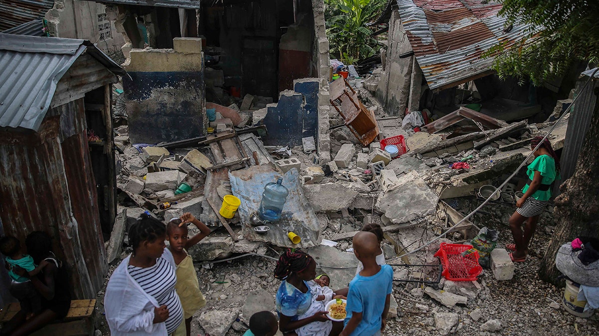 A family eats breakfast in front of homes destroyed by a 7.2 magnitude earthquake in Les Cayes, Haiti, Sunday, Aug. 15, 2021. (AP Photo/Joseph Odelyn)