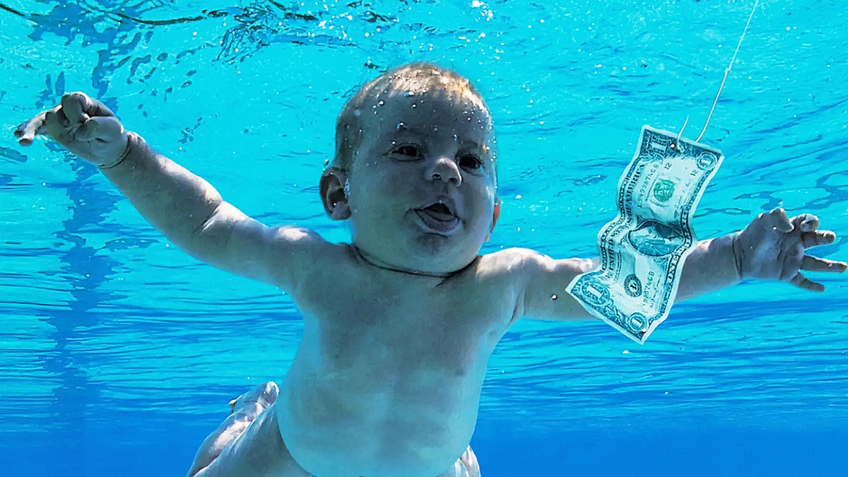 Baby in a pool with a dollar bill floting near it 