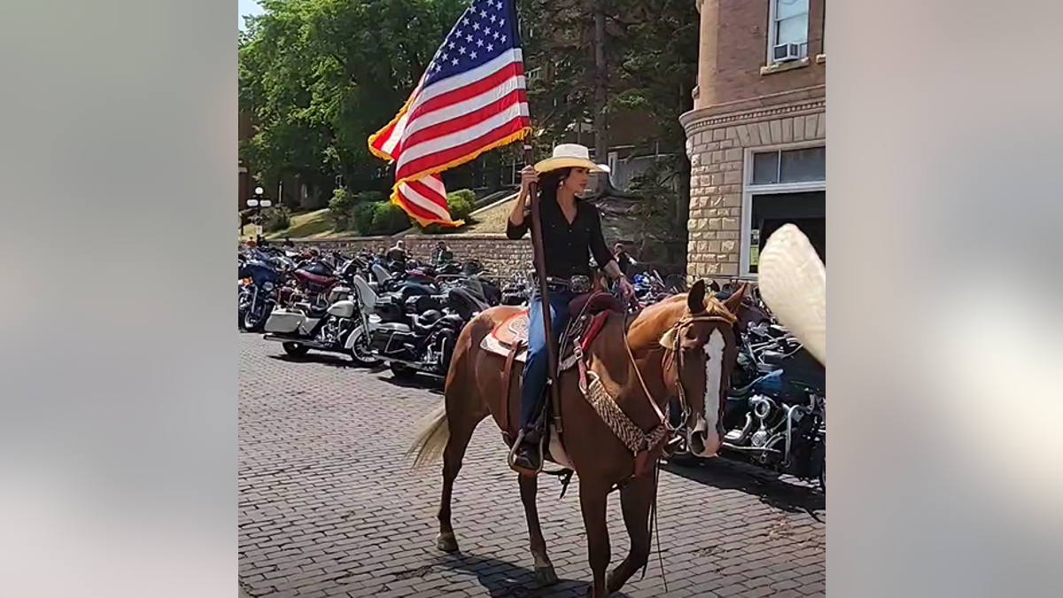 Gov. Kristi Noem carries an American flag on a horse on August 9.