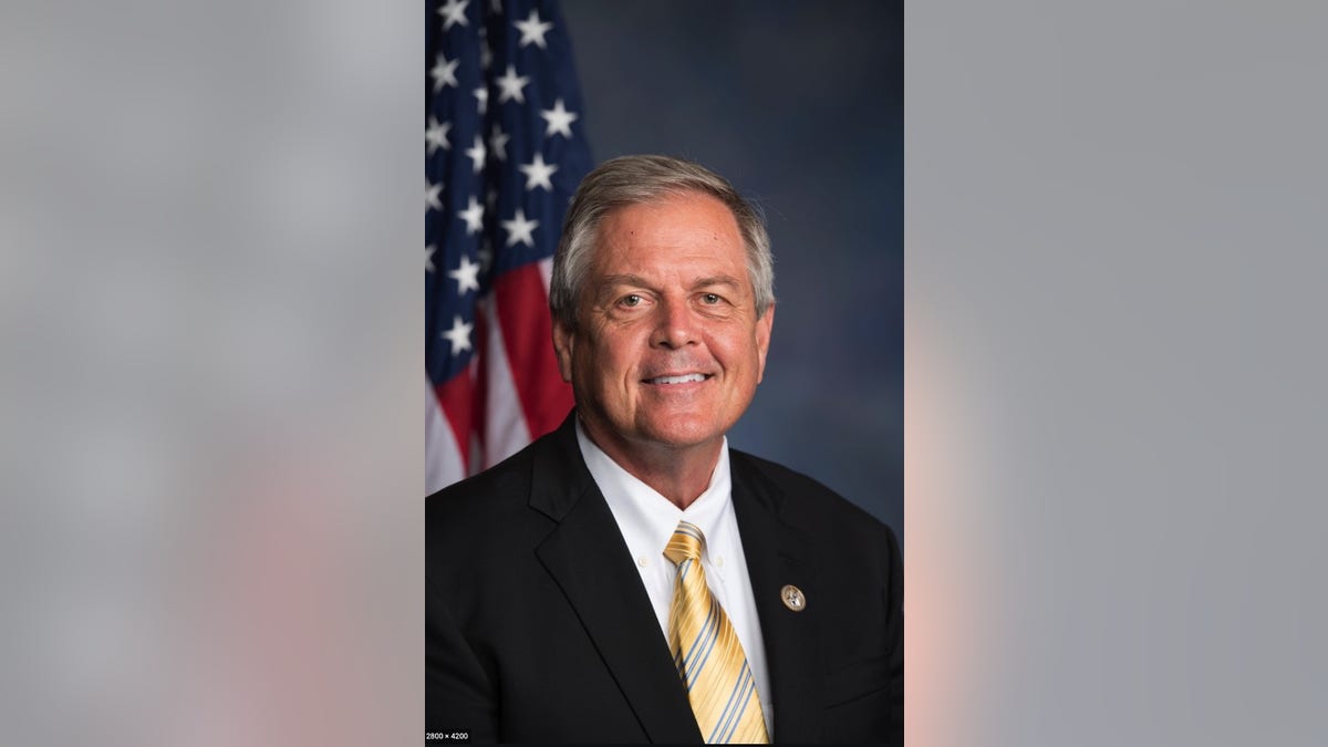 Rep. Ralph Norman, R-S.C. wearing a dark suit, yellow tie, sitting in front of the American flag