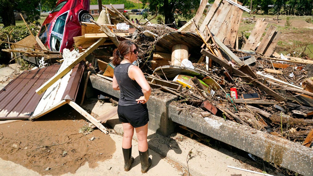 A woman looks at debris washed up against a bridge over a stream Sunday, Aug. 22, 2021, in Waverly, Tenn. Heavy rains caused flooding Saturday in Middle Tennessee and have resulted in multiple deaths as homes and rural roads were washed away.