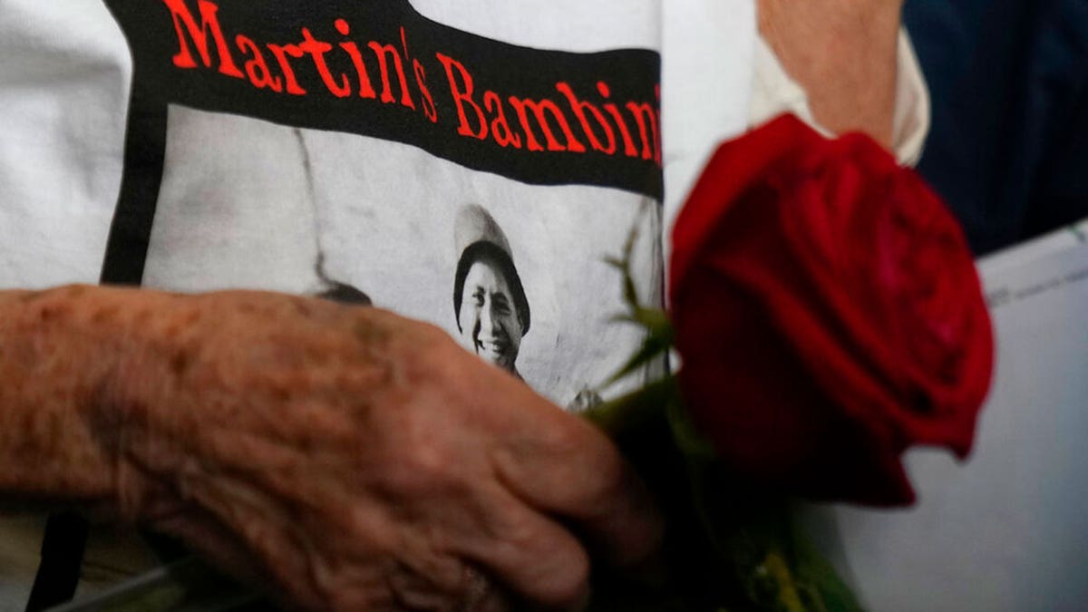 A 97 year old retired American soldier Martin Adler's wife wears a t-shirt with a picture with her husband, Giulio, Mafalda, and Giuliana Naldi taken during a WWII, at Bologna's airport, Italy, Monday, Aug. 23, 2021. For more than seven decades, Martin Adler treasured a back-and-white photo of himself as a young soldier with a broad smile with three impeccably dressed Italian children he is credited with saving as the Nazis retreated northward in 1944. The 97-year-old World War II veteran met the three siblings -- now octogenarians themselves -- in person for the first time on Monday, eight months after a video reunion.