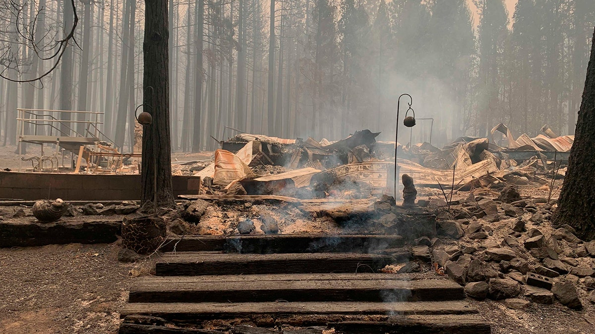 Smoke comes out under the front steps of a house that burned along North Arm Road in Plumas County near Taylorsville, Calif., on Sunday. (AP Photo/Eugene Garcia)