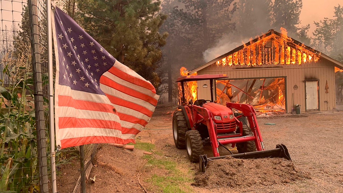 A red tractor is left behind as a home burns outside of Taylorsville in Plumas County, Calif., that was impacted by the Dixie Fire on Friday. (AP Photo/Eugene Garcia)