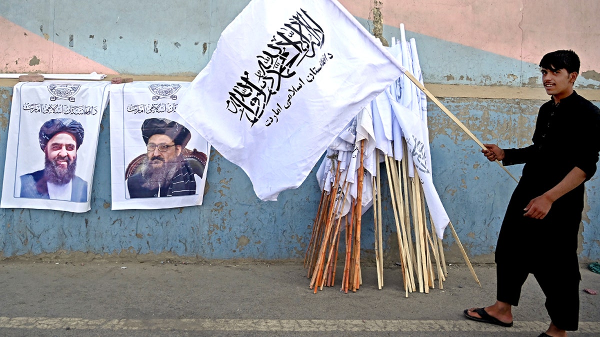 A vendor holds a Taliban flag next to the posters of Taliban leaders Mullah Abdul Ghani Baradar and Amir Khan Muttaqi (L) as he waits for customers along a street in Kabul on August 27, 2021, following the Taliban's military takeover of Afghanistan. (Photo by Aamir QURESHI / AFP) (Photo by AAMIR QURESHI/AFP via Getty Images)