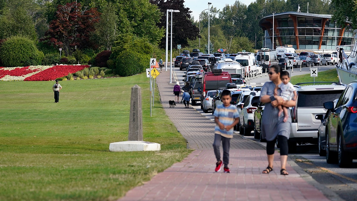 A Canadian border official, left, looks on at line of vehicles waiting to enter Canada at the Peace Arch border crossing Monday, Aug. 9, 2021, in Blaine, Wash. Canada lifted its prohibition on Americans crossing the border to shop, vacation or visit, but America kept similar restrictions in place, part of a bumpy return to normalcy from coronavirus travel bans. (AP Photo/Elaine Thompson)