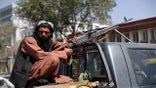 A Taliban fighter sits on the back of a vehicle with a machine gun in front of the main gate leading to the Afghan presidential palace, in Kabul, Afghanistan, on Monday. (AP)