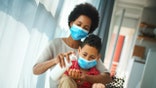 Closeup front iew of an early 40's woman with her son staying at home during coronavirus pandemic. They are staying at home, sitting next to the window. The woman is pouring some hand sanitizer into boys hands.