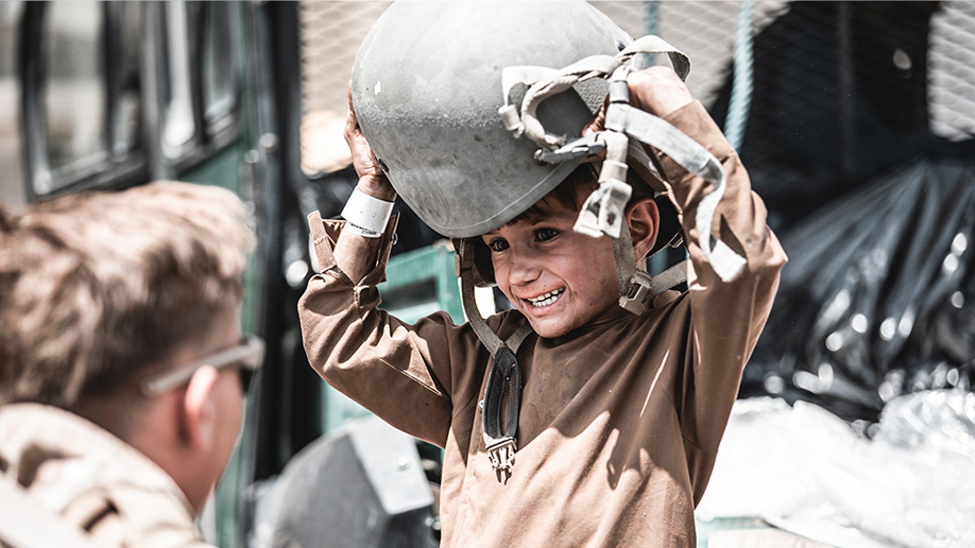 A U.S. Marine assigned to Special Purpose Marine Air-Ground Task Force – Crisis Response – Central Command hands a helmet to a child awaiting evacuation at Hamid Karzai International Airport, Afghanistan, Aug. 22, 2021. The U.S. is assisting the Department of State with a Non-Combatant Evacuation Operation (NEO) in Afghanistan. (U.S. Marine Corps photo by Gunnery Sgt. Melissa Marnell).