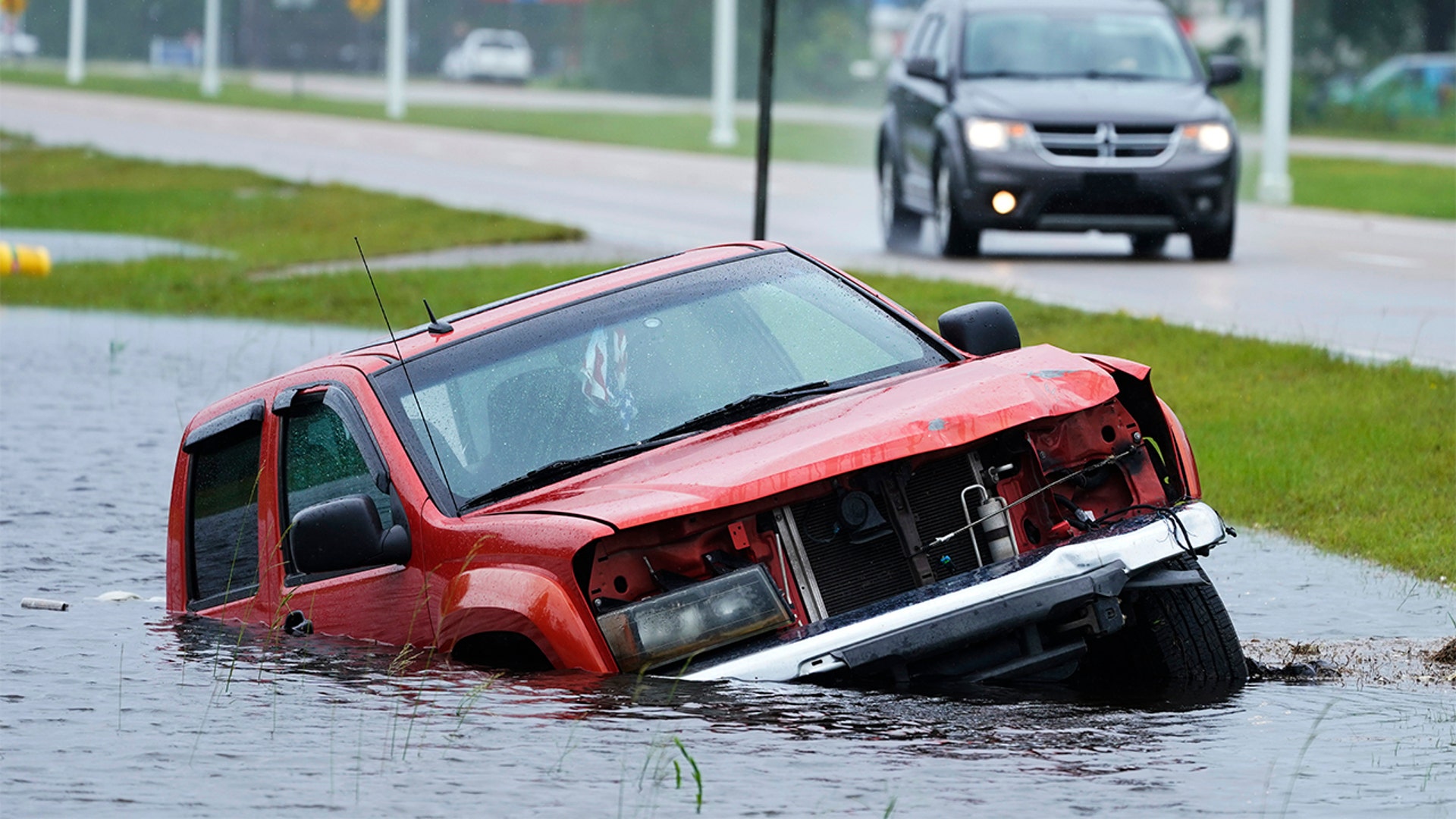 An abandoned vehicle is half submerged in a ditch next to a near flooded highway as the outer bands of Hurricane Ida arrive Sunday, Aug. 29, 2021, in Bay Saint Louis, Miss. (AP Photo/Steve Helber)