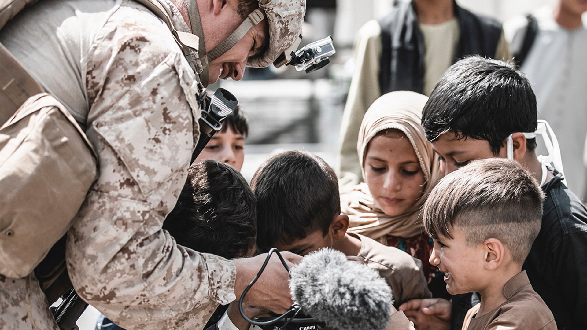 In this Aug. 22, 2021, photo provided by the U.S. Marines, a U.S. Marine assigned to Special Purpose Marine Air-Ground Task Force – Crisis Response – Central Command shows his video camera to children awaiting evacuation at Hamid Karzai International Airport in Kabul, Afghanistan. (Gunnery Sgt. Melissa Marnell/U.S. Marine Corps via AP)