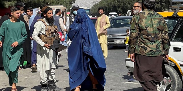 Taliban forces block roads around an airport, while a woman with a Burqa walks by in Kabul, Afghanistan, Aug. 27, 2021. 