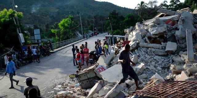 A man walks on a collapsed building in Saint-Louis-du-Sud, Haiti, Monday, Aug. 16, 2021, two days after a 7.2-magnitude earthquake struck the southwestern part of the hemisphere's poorest nation on Aug. 14.(AP Photo/Matias Delacroix)