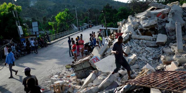 A man walks on a collapsed building in Saint-Louis-du-Sud, Haiti, Monday, Aug. 16, 2021, two days after a 7.2-magnitude earthquake struck the southwestern part of the hemisphere's poorest nation on Aug. 14.(AP Photo/Matias Delacroix)