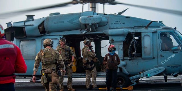 In this photo provided by the U.S. Navy, sailors assigned to an explosive ordnance unit board an MH-60S Seahawk helicopter on the flight deck of aircraft carrier USS Ronald Reagan to head to an oil tanker that was attacked off the coast of Oman in the Arabian Sea on Friday, July 30, 2021.