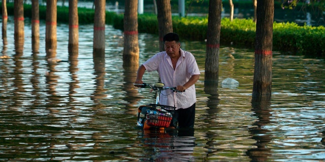 A man pushes a scooter through floodwaters in Xinxiang in central China's Henan Province, Monday, on July 26, 2021. (AP Photo/Dake Kang, File)