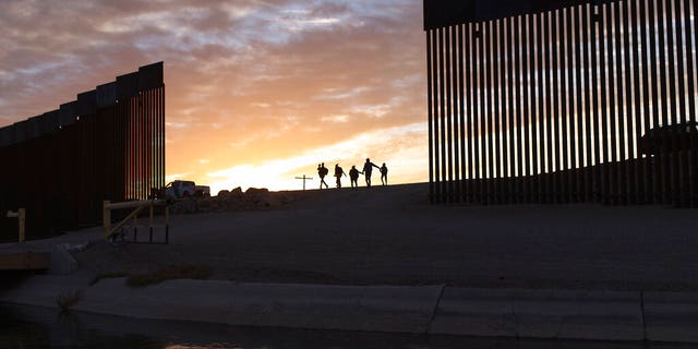 A pair of migrant families from Brazil pass through a gap in the border wall to reach the United States after crossing from Mexico to Yuma, Ariz., to seek asylum, in June 2021.   